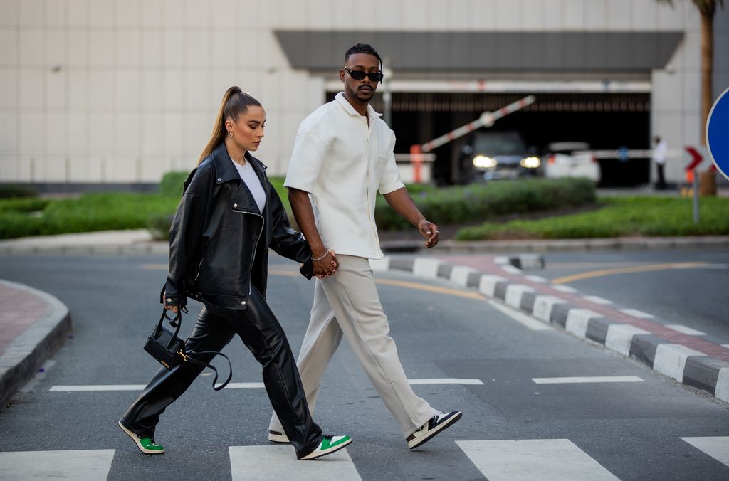 DUBAI, UNITED ARAB EMIRATES - DECEMBER 12: Couple Anna Idriess is seen wearing leather pants ZARA, white top von ZARA, jacket WRSTBHVR, sneaker NIKE, micro bag Jacquemus and Mubi Idriess wearing button shirt Worst-Behaviour, pants Cos, Sneaker: Nike on December 12, 2021 in Dubai, United Arab Emirates. (Photo by Christian Vierig/Getty Images)
