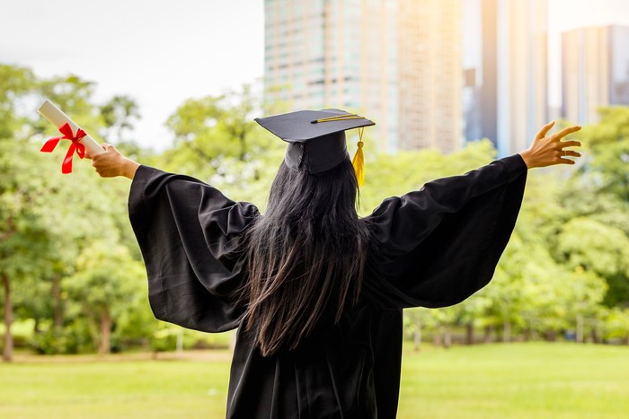 Successful graduating student wearing cap and gown holding diploma