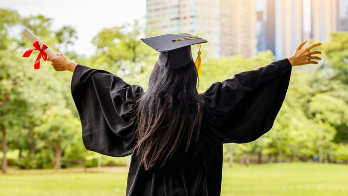 Successful graduating student wearing cap and gown holding diploma