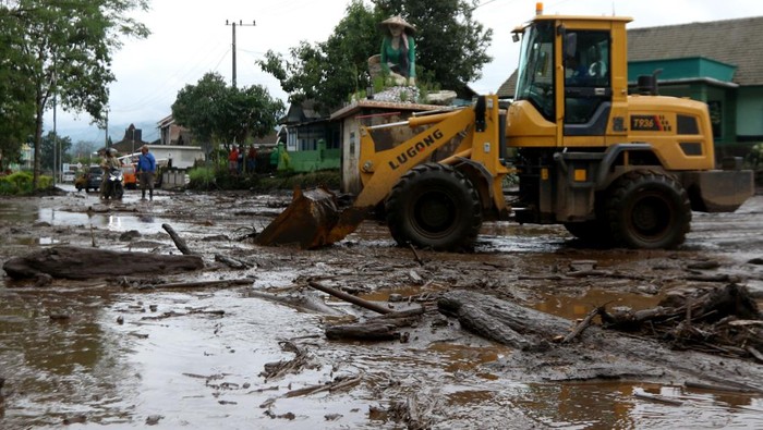Petugas menggunakan alat berat membersihkan material lumpur dan kayu yang menutupi jalan di Desa Sempol, Ijen, Bondowoso, Jawa Timur, Senin (13/2/2023). Terjadi banjir bandang susulan pada sore hari yang menyebabkan terganggunya jalur lalulintas  penghubung Bondowoso-Banyuwangi karena terendam material lumpur. Hingga saat ini petugas masih membersihkan jalan tersebut. ANTARA FOTO/Budi Candra Setya/