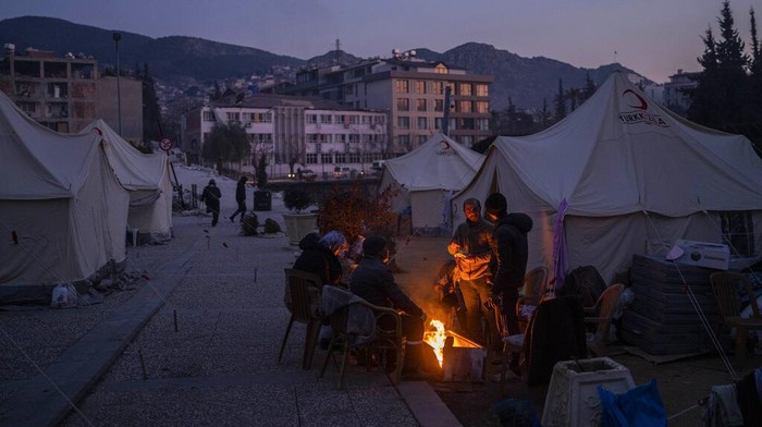 People gather around a bonfire at a temporary camp for residents who lost their homes during the earthquake in Antakya, southeastern Turkey, Monday, Feb. 13, 2023. Thousands left homeless by a massive earthquake that struck Turkey and Syria a week ago packed into crowded tents or lined up in the streets Monday for hot meals as the desperate search for survivors entered what was likely its last hours. (AP Photo/Bernat Armangue)