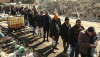 Orang-orang mengantre untuk mendapatkan air di dekat bangunan yang runtuh di Kahramanmaras, Turki selatan. AP/Emrah Gurel  