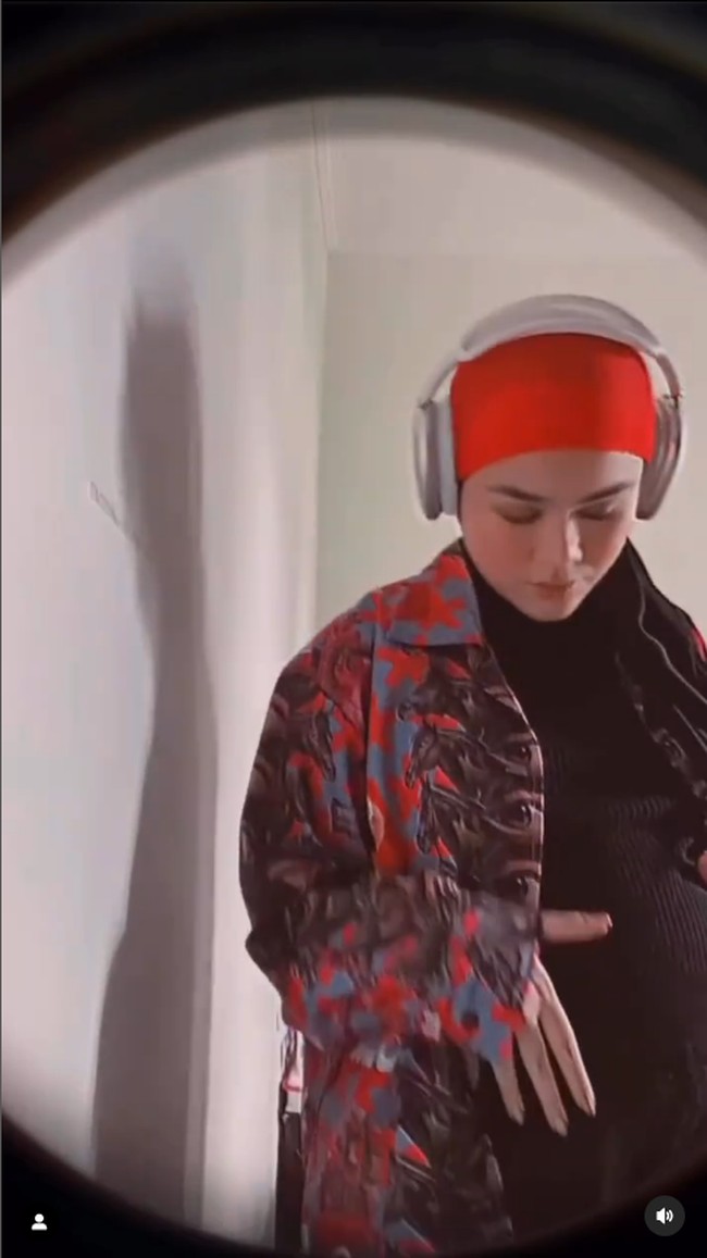 Dalam unggahannya Sivia memperlihatkan momennya mengelus perutnya yang semakin membesar.  Sivia bergaya boyish memakai turban oranye, kemeja oversized dan headphone di kepalanya. Foto: Dok. Instagram @siviazizah.