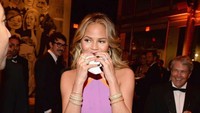 Chrissy Teigen seolah tak memedulikan acara yang ia sambangi. Ia yang mengenakan dress ungu tampak lahap makan burger meski jadi sorotan tamu lain.
