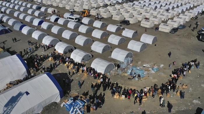 People who lost their houses in the devastating earthquake, lineup to receive food at a makeshift camp, in Iskenderun city, southern Turkey, Tuesday, Feb. 14, 2023. Thousands left homeless by a massive earthquake that struck Turkey and Syria a week ago packed into crowded tents or lined up in the streets for hot meals as the desperate search for survivors entered what was likely its last hours. (AP Photo/Hussein Malla)