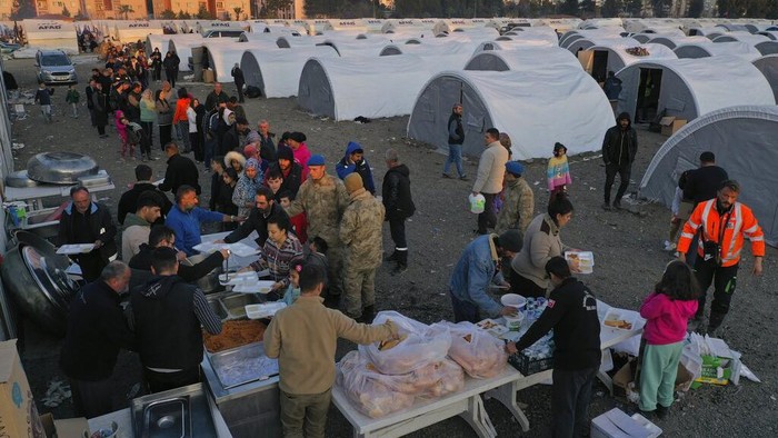 People who lost their houses in the devastating earthquake, lineup to receive food at a makeshift camp, in Iskenderun city, southern Turkey, Tuesday, Feb. 14, 2023. Thousands left homeless by a massive earthquake that struck Turkey and Syria a week ago packed into crowded tents or lined up in the streets for hot meals as the desperate search for survivors entered what was likely its last hours. (AP Photo/Hussein Malla)