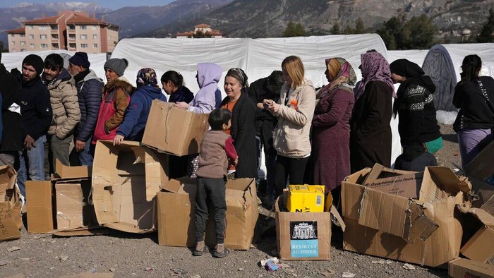 Potret Aktivitas Korban Gempa Turki di Pengungsian People who lost their houses in the devastating earthquake, lineup to receive food at a makeshift camp, in Iskenderun city, southern Turkey, Tuesday, Feb. 14, 2023. Thousands left homeless by a massive earthquake that struck Turkey and Syria a week ago packed into crowded tents or lined up in the streets for hot meals as the desperate search for survivors entered what was likely its last hours. (AP Photo/Hussein Malla)