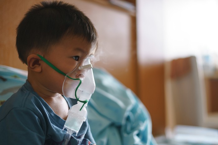 Sick Asian boy about 2 years and 8 months in hospital using inhaler containing medicine to stop coughing from disease like flu or RSV, Respiratory Syncytial Virus