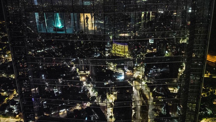 A man walks on the Costanera shopping center lookout, as the city is reflected in the windows of the building after sunset in Santiago, Chile, Thursday, Jan. 19, 2023. (AP Photo/Matias Delacroix)