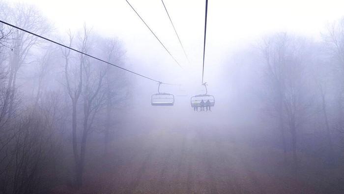 Bingkai Sepekan: Menembus Cahaya Memaku Ruang Skiers ride the Gunnar chairlift through heavy fog above a bare Gunnar Chair Line Slope at Seven Springs Mountain Resort in Champion, Pa., Wednesday, Jan. 18, 2023. The resort currently has 47% of its terrain open due to warm and rainy winter. (John Rucosky/The Tribune-Democrat via AP)