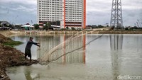 Tampak seorang warga menjaring ikan di Waduk Belibis.