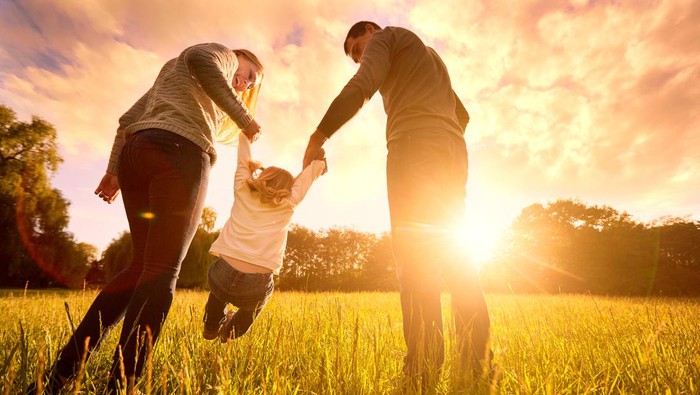 Happy family in the park evening light. The lights of a sun. Mom, dad and baby happy walk at sunset. The concept of a happy family.Parents hold the babys hands.