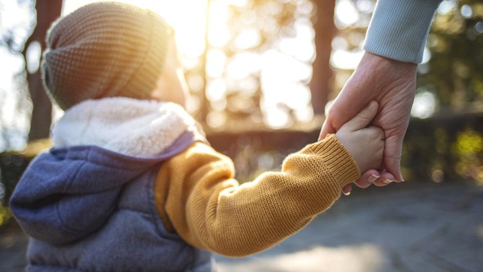 Happy family in the park evening light. The lights of a sun. Mom, dad and baby happy walk at sunset. The concept of a happy family.Parents hold the babys hands.
