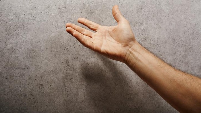 Male hand raised in front of a gray wall pleading