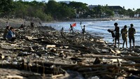 Orang-orang duduk di antara puing-puing dan sampah yang terdampar di Pantai Kuta, Bali, Sabtu (18/2/2023). 