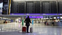 Seorang penumpang dengan barang bawaannya berdiri di sebuah papan informasi jadwal penerbangan di Bandara Frankfurt, Jerman, Jumat (17/2/2023).  