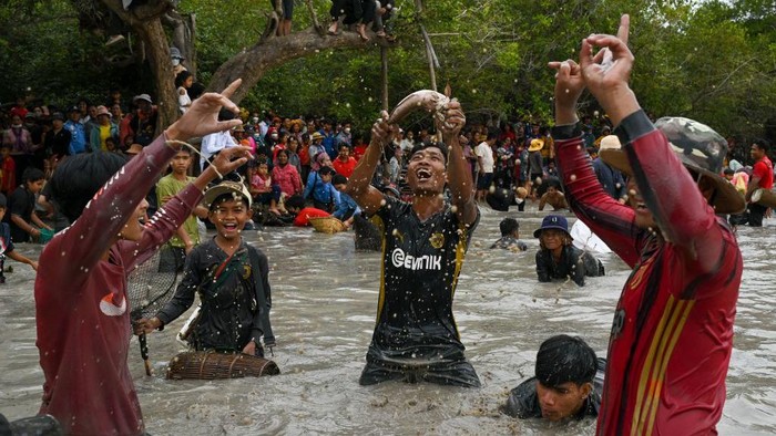Serunya Tradisi Menangkap Ikan di Kamboja A Cambodian man (C) holds up a snake fish during the annual fish-catching ceremony at the Choam Krovean commune in Tboung Khmum province on February 18, 2023. - Wielding handmade bamboo baskets and nylon nets, hundreds of people waded thigh-deep into a muddy lake in eastern Cambodia on Saturday for the annual fish-catching ceremony, during which only traditional tools were used. (Photo by TANG CHHIN SOTHY / AFP) (Photo by TANG CHHIN SOTHY/AFP via Getty Images)