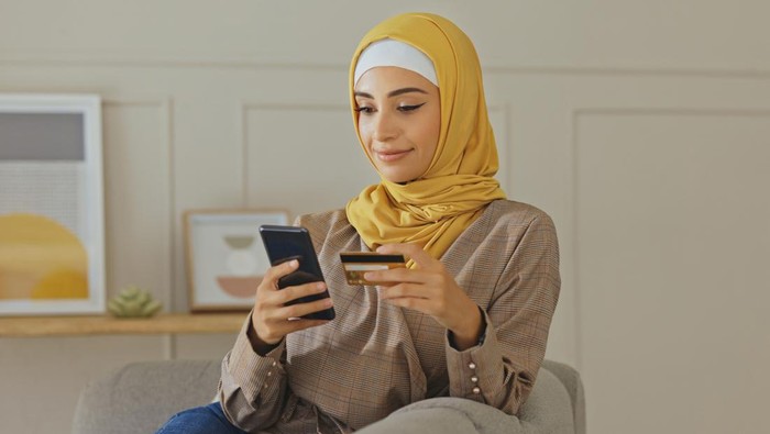 Credit card, muslim or woman with phone on online shopping or payment, internet purchase or ecommerce in living room. Fintech, happy or Islamic girl hands on smartphone for trading, banking or invest