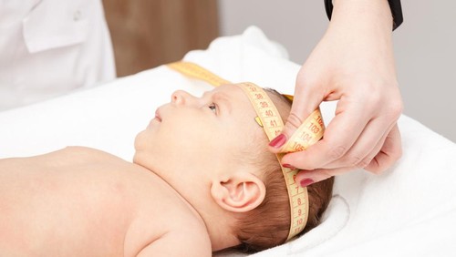 Close-up shot of pediatrician examines two months baby boy. Doctor using measurement tape checking baby head size