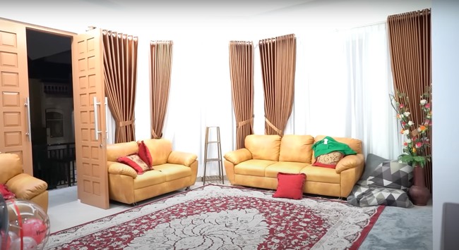 Masuk ke bagian dalam rumah terlihat ruang tamu yang cukup luas. Didominasi warna coklat, ruang tamu di rumah Haji Faisal tampak nyaman dengan dilengkapi sofa dan juga karpet. Foto: YouTube/Fuji an