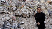 Annalena Baerbock berdiri dengan latar belakang bangunan yang hancur akibat gempa di Kahramanmaras.