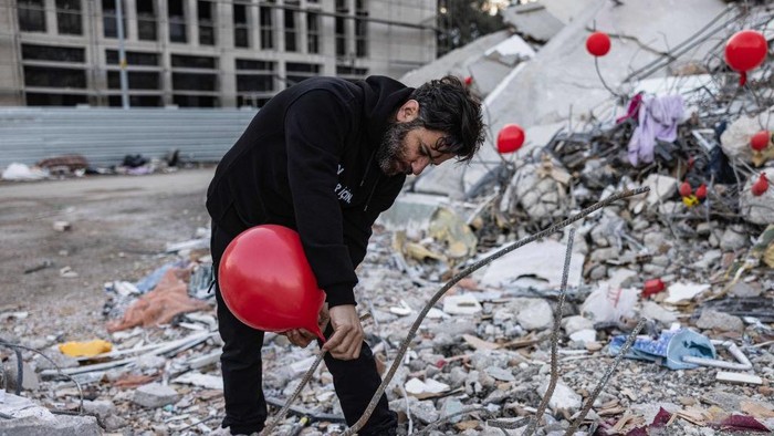 Balon Merah Hiasi Reruntuhan Gempa Turki, Kenang Korban Tewas Ogun Sever Okur, 38-year-old Turkish man hangs a ballon on the debris of a collapsed building in Antakya, southern Turkey on February 21, 2023, following the 6.4-magnitude earthquake which struck on February 20, two weeks after a 7.8-magnitude earthquake hit near Gaziantep and has killed more than 44,000 people. - On the side of a busy road in Antakya, dozens of red balloons flutter around, hanging from the ruins. They are