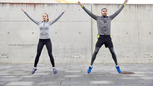 fitness, sport, people, exercising and lifestyle concept - happy man and woman doing jumping jack or star jump exercise outdoors