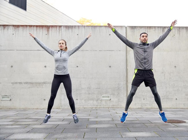 fitness, sport, people, exercising and lifestyle concept - happy man and woman doing jumping jack or star jump exercise outdoors