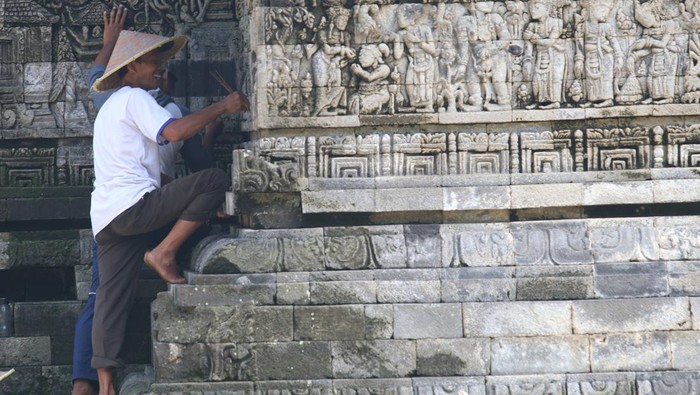 Pekerja membersihkan lumut yang tumbuh pada relief candi Tegowangi menggunakan lidi di Desa Tegowangi, Kediri, Jawa Timur, Selasa (21/2/2023). Candi Hindu yang dibangun pada masa Kerajaan Majapahit sekitar tahun 1400 masehi tersebut dibersihkan lumutnya secara berkelanjutan guna mencegah keroposnya relief terutama saat musim hujan. ANTARA FOTO/Prasetia Fauzani/foc.