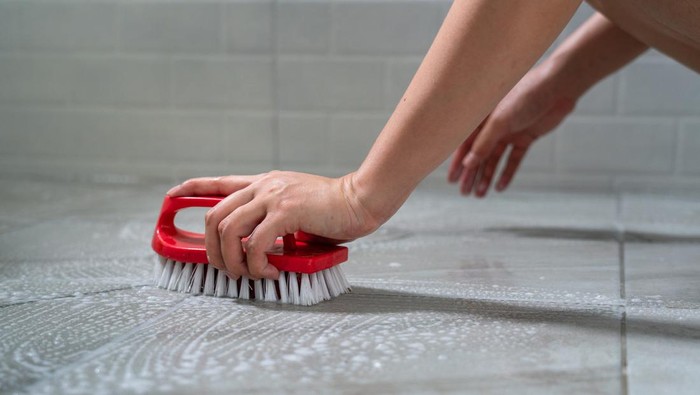 Action of a humans hand is using floor brush to cleaning toilet marble tile floor. Close-up and selective focus at hand part.