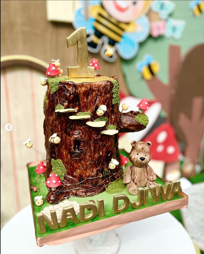 Kue ulang tahun baby Djiwa juga tampak cukup unik. Sesuai dengan tema ulang tahunnya, kue tersebut berbentuk seperti batang pohon yang dihinggapi oleh beberapa lebah kecil. Pada bagian atasnya terdapat angka 1 yang melambangkan usia baby Djiwa. Dan pada bagian depannya tertulis nama Nadi Djiwa. Foto: Instagram/@nadinelist