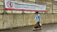 Warga melintas di depan spanduk larangan kencing sembarangan di tembok jalur pedestrian di Jl Lebak Bulus Raya, tak jauh dari Stasiun MRT Lebak Bulus, Jakarta, Jumat (24/2/2023).