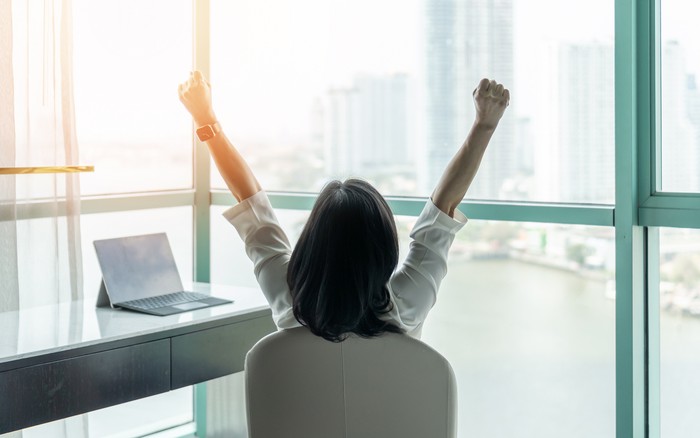 Ilustrasi Bahagia Setelah Bercerai Business achievement concept with happy businesswoman relaxing in office or hotel room, resting and raising fists with ambition looking forward to city building urban scene through glass window