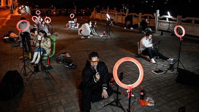 The photo taken on February 20, 2023 shows outdoor livestreamers singing and chatting with the audiences through their mobile phones on an overpass bridge at night in Guilin, in southern China's Guangxi province. - In the dead of night on a bridge in southern China, around two dozen livestreamers sat crooning and chatting into microphones, their identical ring lights spaced a few metres apart in glowing rows. (Photo by Jade GAO / AFP) / To go with 