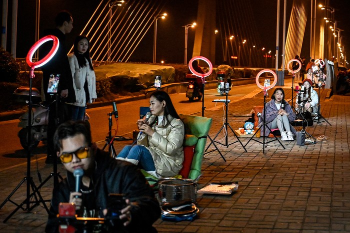 The photo taken on February 20, 2023 shows outdoor livestreamers singing and chatting with the audiences through their mobile phones on an overpass bridge at night in Guilin, in southern Chinas Guangxi province. - In the dead of night on a bridge in southern China, around two dozen livestreamers sat crooning and chatting into microphones, their identical ring lights spaced a few metres apart in glowing rows. (Photo by Jade GAO / AFP) / To go with 
