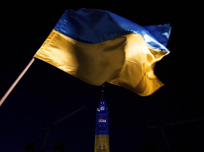 The Ukrainian flag is seen as Centre Block of Parliament Hill is illuminated in the Ukrainian colors of blue and yellow during a vigil marking one year since the Russian invasion of Ukraine on Parliament Hill in Ottawa, Ontario, Friday, Feb. 24, 2023