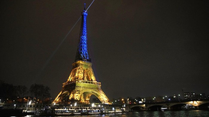 Setahun Invasi Rusia, Sederet Ikon Dunia Diterangi Bendera Ukraina The Eiffel Tower is illuminated with the colors of Ukraine to mark the one-year anniversary of Russia's invasion of the country, in Paris, Thursday, Jan. 23, 2023. (AP Photo/Christophe Ena)