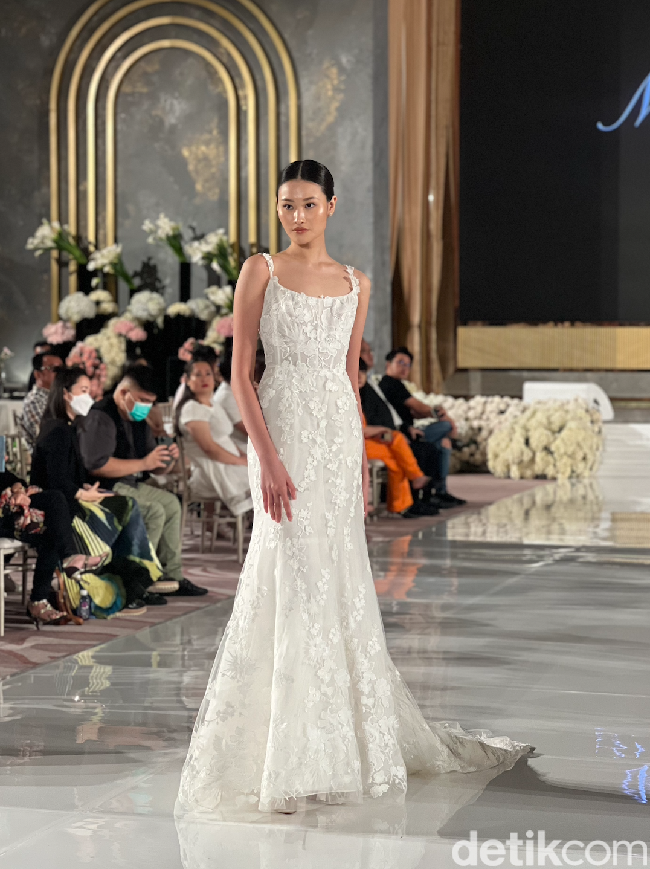 Gaun pengantin ini merupakan rancangan desainer Monique Lhuillier. Berbentuk mermaid dan tanpa lengan, gaun pengantin ini bisa membuat penampilan calon memperlai jadi terlihat langsing dan tinggi. Desainnya pun tampak simpel dengan sedikit buntut pada bagian belakangnya. Aksen bunga yang senada pada gaun kian mempercantik tampilan. Foto: Wolipop/Vina Oktiani