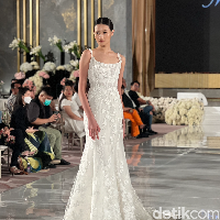 Gaun pengantin ini merupakan rancangan desainer Monique Lhuillier. Berbentuk mermaid dan tanpa lengan, gaun pengantin ini bisa membuat penampilan calon memperlai jadi terlihat langsing dan tinggi. Desainnya pun tampak simpel dengan sedikit buntut pada bagian belakangnya. Aksen bunga yang senada pada gaun kian mempercantik tampilan. Foto: Wolipop/Vina Oktiani