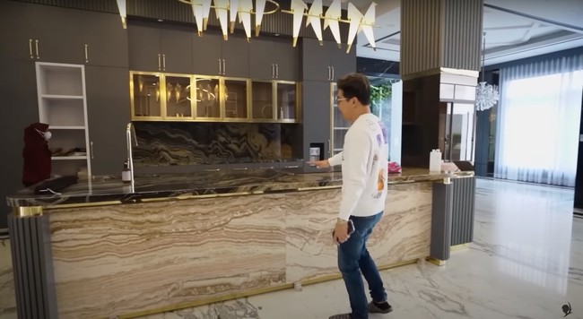 Di dekat ruang keluarga terdapat dapur kering yang desainnya tak kalah cantik dengan didominasi warna hitam dan gold. Di dapur tersebut terdapat sebuah kulkas seharga Rp 60 juta. Tak hanya itu saja, meja dapurnya itu juga disebut dokter Richard terbuat dari batu yang berasal dari Brazil. Foto: YouTube/dr. Richard Lee, MARS