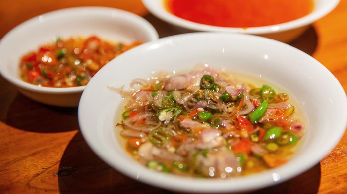 Close up shot of delicious spicy Balinese raw chili chopped with shallot and lemongrass ( sambal matah bali ). Theres various chili condiment on the side.
