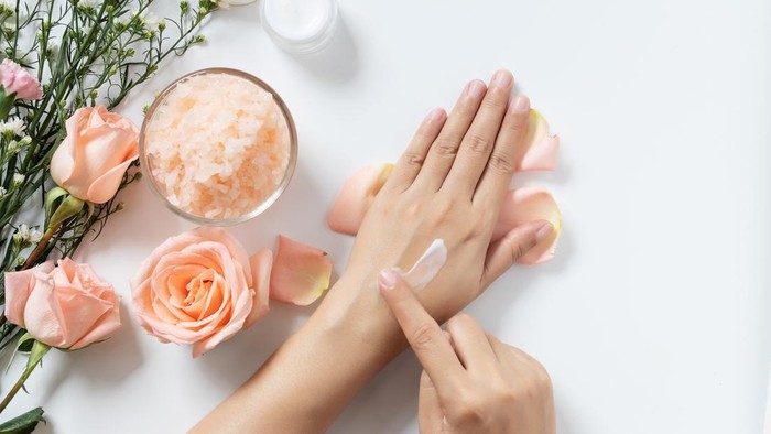 natural skincare concept. woman apply white cream on her hands on white background with jar of cosmetic cream, salt spa scrub ,rose and  white flowers with copy space