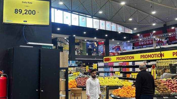 Customers walk past a screen showing the daily U.S. dollar rate at a supermarket in Beirut, Wednesday, March 1, 2023. Lebanon began pricing goods in supermarkets in U.S. dollars Wednesday as the value of the Lebanese pound hit new lows. (AP Photo/Hussein Malla)