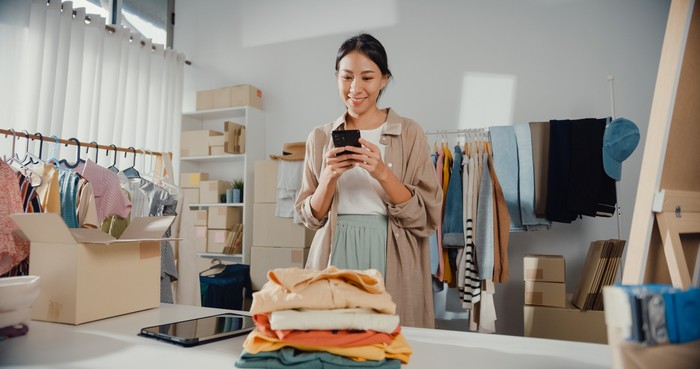 Young Asian business owner woman use smartphone check order purchase online in home.