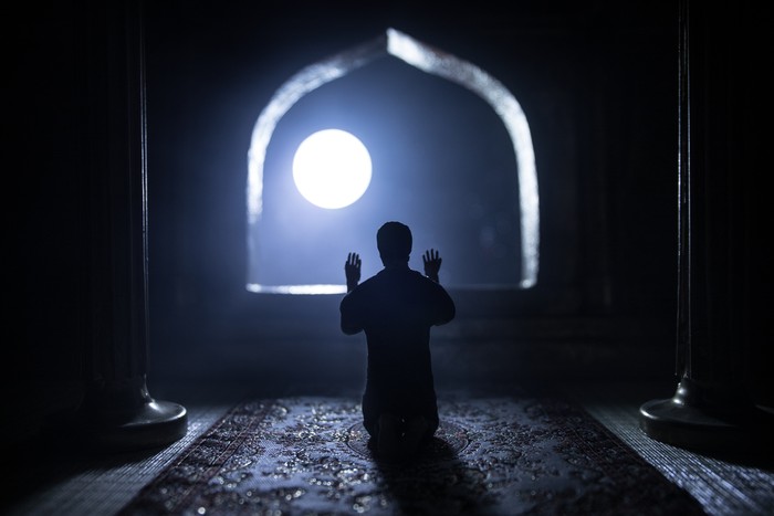 A realistic Arabian interior miniature with window and columns. Silhouette of muslim praying on carpet near window. Festive greeting card, invitation for Muslim holy month Ramadan Kareem. Selective focus