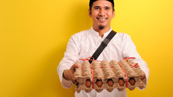 In Ramadan Kareem, Smiling Happy Young Asian Muslim man bring  a plate of eggs to give for everyone need, isolated on yellow background