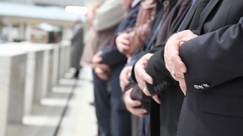 Close Up Shot of Muslim People Tied Hands. One Persons Hand on Foreground is in Focus and the Others on Background is Out of Focus. Coffins also in front of the People. Islamic Ceremony for Dead People. Whorshippers Standing next to the Coffins and Pray.