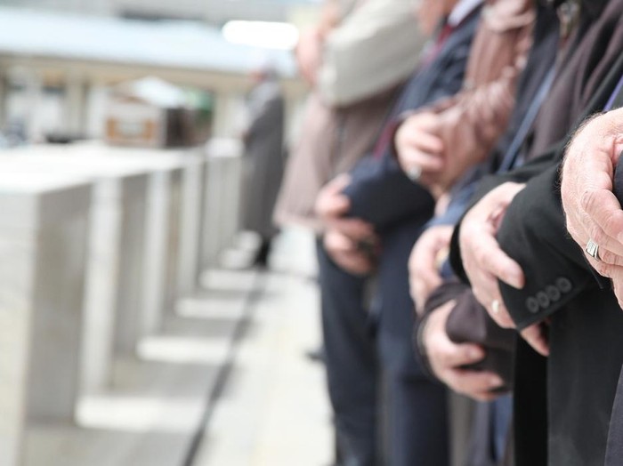 Close Up Shot of Muslim People Tied Hands. One Persons Hand on Foreground is in Focus and the Others on Background is Out of Focus. Coffins also in front of the People. Islamic Ceremony for Dead People. Whorshippers Standing next to the Coffins and Pray.