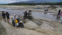 Warga menggunakan sepeda motor melintasi jalan yang terputus akibat digerus air sungai di Desa Sibalaya Barat, Sigi, Sulawesi Tengah, Sabtu (4/3/2023).