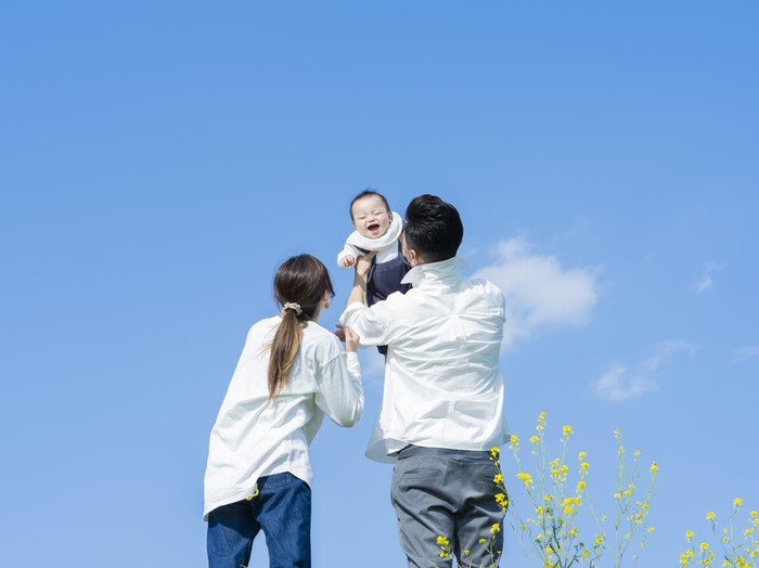 Parents holding their baby high under the blue sky
